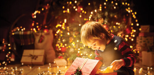 Christmas Child Open Present Gift, Happy Baby Boy looking to Magic Light in Box, Kid sitting front of Xmas Tree