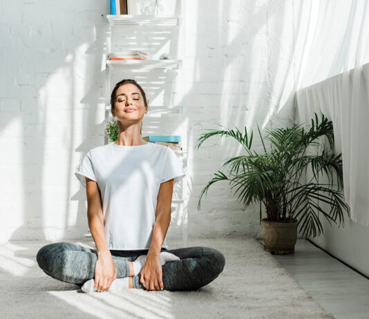 beautiful happy woman with closed eyes practicing yoga in lotus position in bedroom in the morning