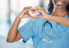 Closeup african american woman nurse making a heart shape with her hands while smiling and standing in hospital. Take care of your heart and love your body. Health and safety in the field of medicine