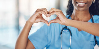 Closeup african american woman nurse making a heart shape with her hands while smiling and standing in hospital. Take care of your heart and love your body. Health and safety in the field of medicine