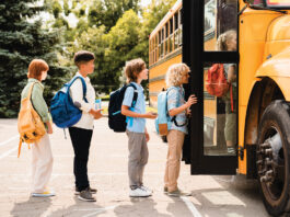 Multiethnic mixed-race pupils classmates schoolchildren students standing in line waiting for boarding school bus before starting new educational semester year after summer holidays