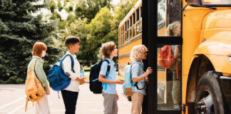 Multiethnic mixed-race pupils classmates schoolchildren students standing in line waiting for boarding school bus before starting new educational semester year after summer holidays