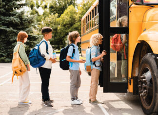 Multiethnic mixed-race pupils classmates schoolchildren students standing in line waiting for boarding school bus before starting new educational semester year after summer holidays