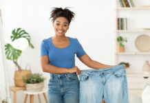 Happy Slim Black Girl Showing Old Jeans Standing At Home