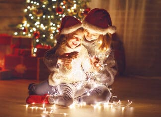 You Are a Holiday Hero When You Help Those In Need Merry Christmas! mother and child daughter with a glowing Christmas garland near tree