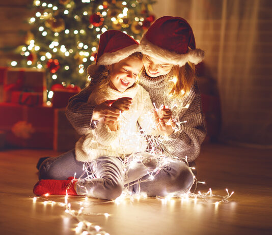 Merry Christmas! mother and child daughter with a glowing Christmas garland near tree