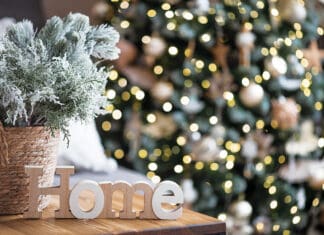 Merry Christmas, Happy Hanukkah, Blessed Ramadan & Kwanzaa Greetings! Beautiful holiday card. The concept of a happy new year and Christmas 2024. Christmas trees and a home sign on a wooden table in a cozy living room.