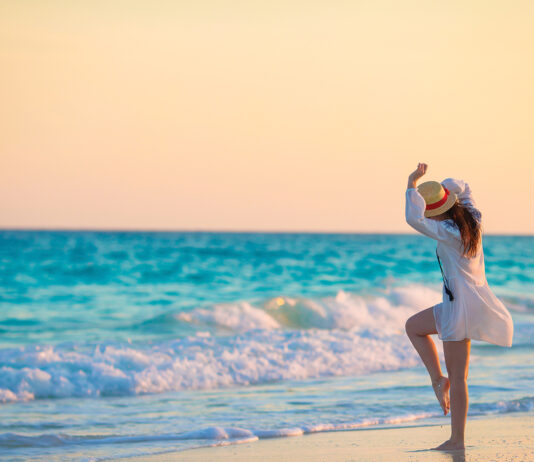 Young happy woman in swimsuit on white beach