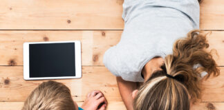 Top view image of two kids lying on the floor and playing with tablet and smartphone watching movie or gaming.