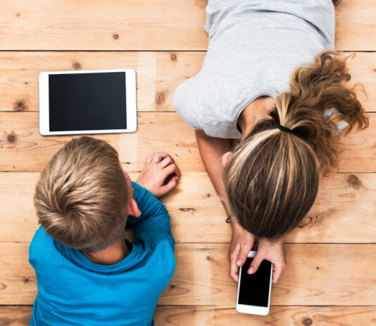 Top view image of two kids lying on the floor and playing with tablet and smartphone watching movie or gaming.