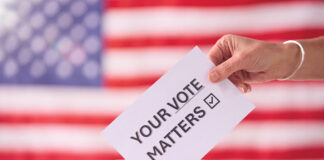 Hand Placing Ballot in Box With American Flag