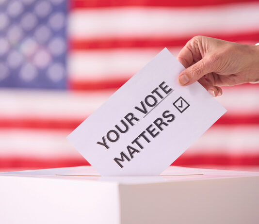 Hand Placing Ballot in Box With American Flag