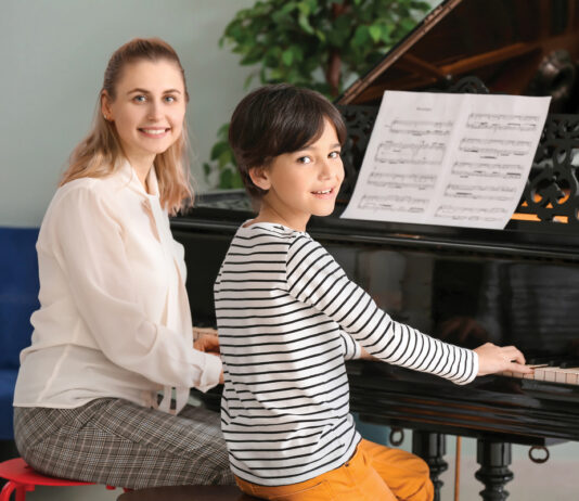 Private music teacher giving piano lessons to little boy