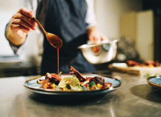 Chef pouring special sauce on pork ribs in the kitchen