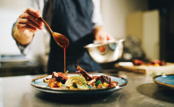 Chef pouring special sauce on pork ribs in the kitchen