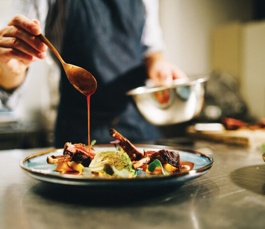 Chef pouring special sauce on pork ribs in the kitchen