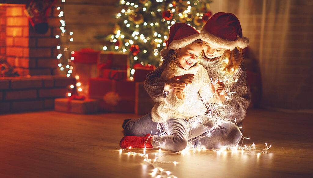 Merry Christmas! mother and child daughter with glowing garland near tree