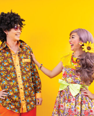 Asian hippie couple dress in 80s colorful vintage fashion with retro clothing while dancing together isolated on yellow background for fancy outfit party and pop culture