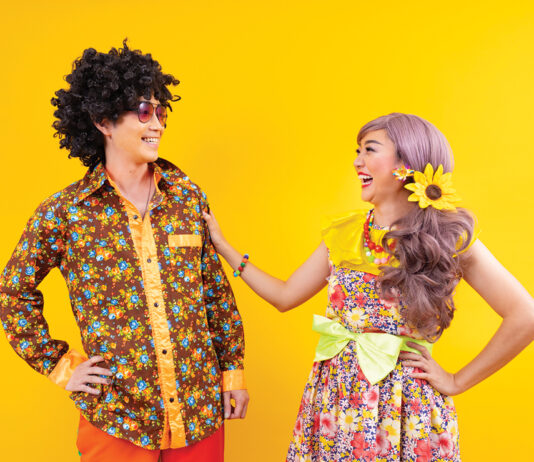 Asian hippie couple dress in 80s colorful vintage fashion with retro clothing while dancing together isolated on yellow background for fancy outfit party and pop culture