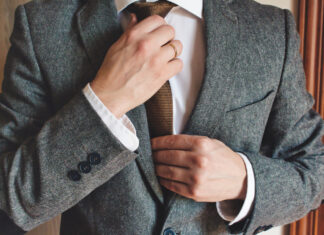 Man in smart suit wearing wedding ring adjusting tie. Elegant tailor-made clothing.