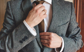 Man in smart suit wearing wedding ring adjusting tie. Elegant tailor-made clothing.