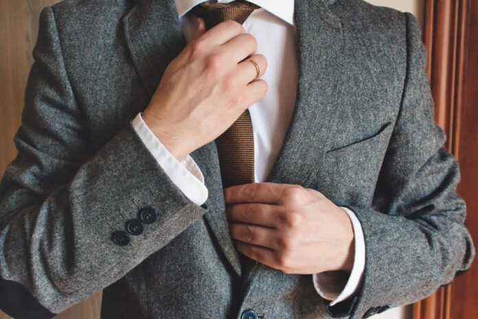 Man in smart suit wearing wedding ring adjusting tie. Elegant tailor-made clothing.