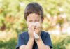 Allergic child sneezing covering nose with wipe in a park in spring or summer season