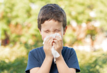 Allergic child sneezing covering nose with wipe in a park in spring or summer season