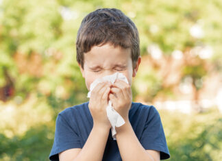 Allergic child sneezing covering nose with wipe in a park in spring or summer season