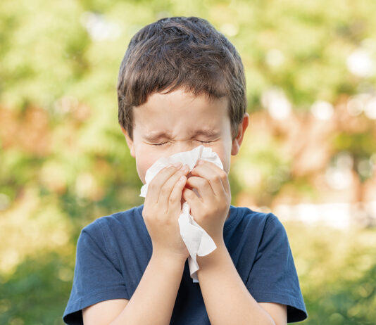 Allergic child sneezing covering nose with wipe in a park in spring or summer season