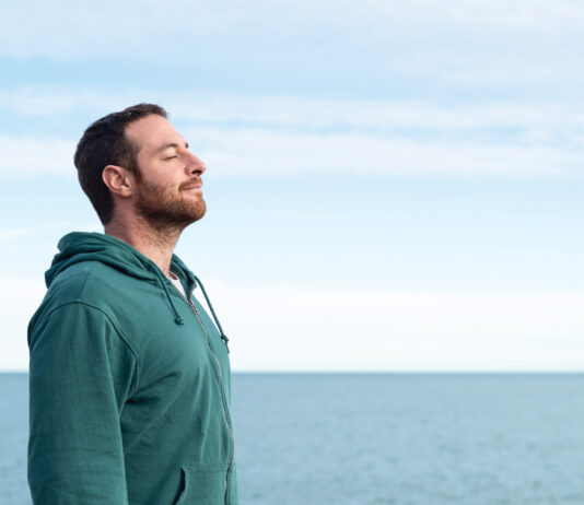 Relaxed man breathing fresh air with the sea at the background.