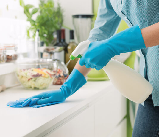 Woman cleaning and polishing the kitchen worktop with a spray detergent, housekeeping and hygiene concept