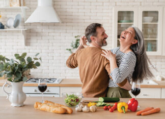 Happy cheerful middle-aged mature couple family parents dancing together in the kitchen, preparing cooking food meal for romantic dinner, spending time together. Active seniors