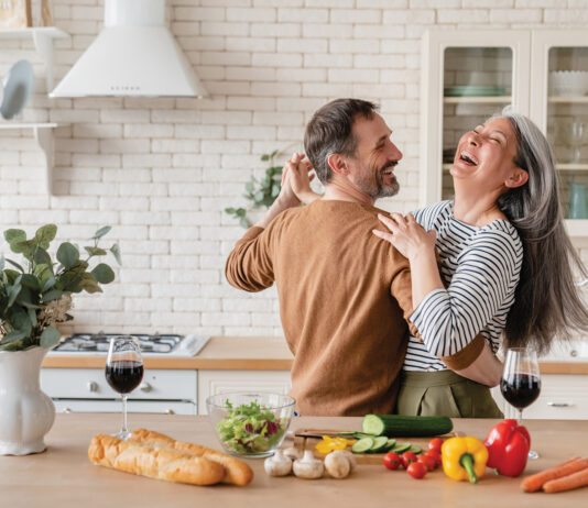 Happy cheerful middle-aged mature couple family parents dancing together in the kitchen, preparing cooking food meal for romantic dinner, spending time together. Active seniors