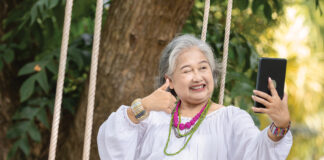 Elderly Woman Relaxing on a Swing While Using a Tablet in a Serene Outdoor Setting, Surrounded by Lush Greenery and Natural Beauty