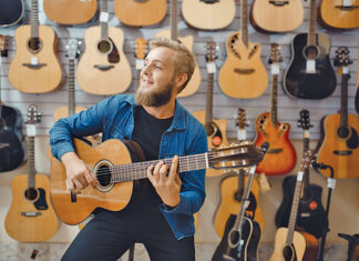Young man plays on acoustic guitar in music store. Assortment in musical instruments shop, male musician buying equipment