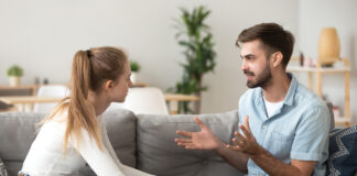 Serious young couple sitting together on sofa, talking about relationships, spending time together at home, focused wife listening to speaking husband, friends having conversation