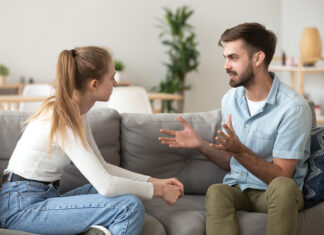 Serious young couple sitting together on sofa, talking about relationships, spending time together at home, focused wife listening to speaking husband, friends having conversation