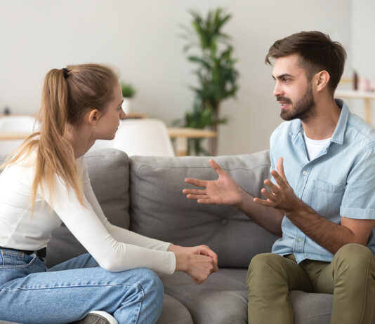 Serious young couple sitting together on sofa, talking about relationships, spending time together at home, focused wife listening to speaking husband, friends having conversation